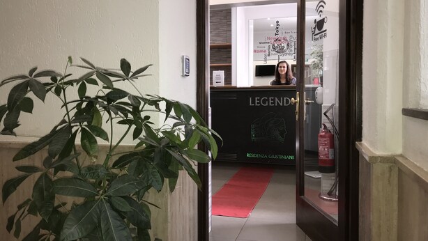 A hotel reception area with a receptionist, a plant, and a sign that reads "LEGEND". - Legend R. G. (Rome)