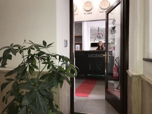 Un'area reception di un hotel con una receptionist, una pianta e un cartello con scritto “LEGEND”.