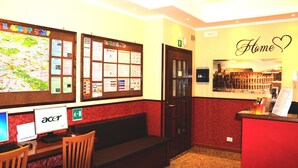 A reception area with a desk, chairs, a bulletin board with various notices, and a 'Home' sign on the wall. - Legend R. G. (Rome)