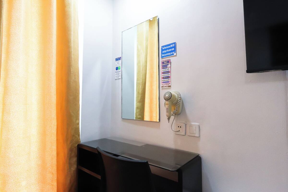 Ein Hotelzimmer mit Schreibtisch, Spiegel, Föhn und an der Wand befestigtem Fernseher.
