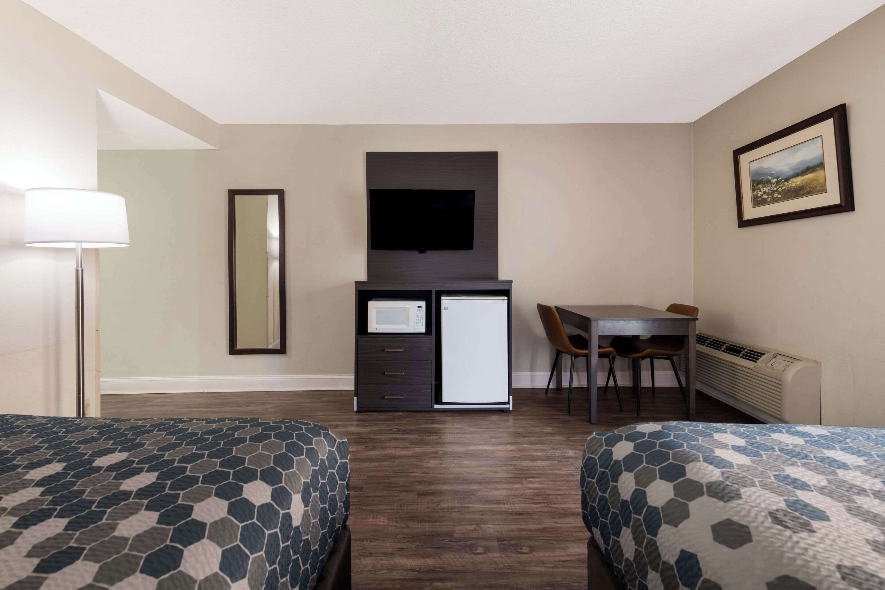 A hotel room with two beds, a desk, a chair, a flat-screen TV, a microwave, a mini-fridge, a lamp, and a framed picture on the wall.