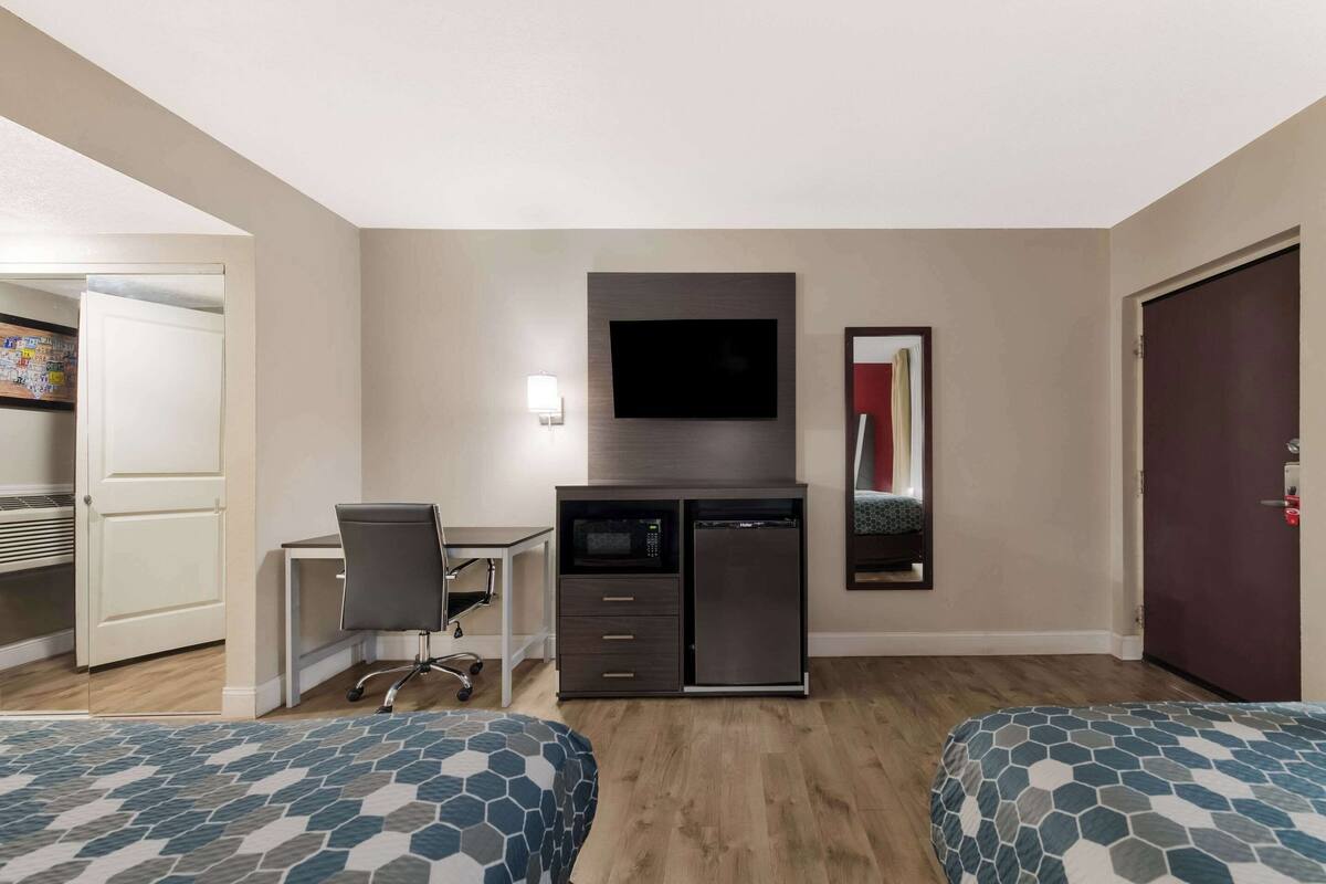 Ein Hotelzimmer mit zwei Betten, einem Schreibtisch mit Stuhl, einem Fernseher, einer Mikrowelle und einem Kühlschrank.