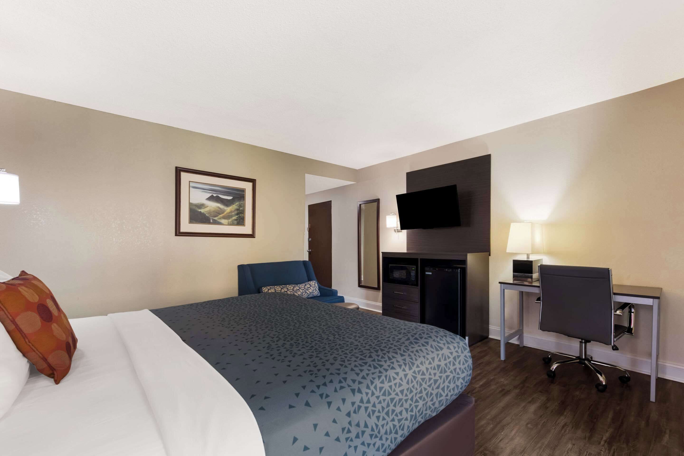 Una habitación de hotel con cama, escritorio, silla, televisor y lámpara.