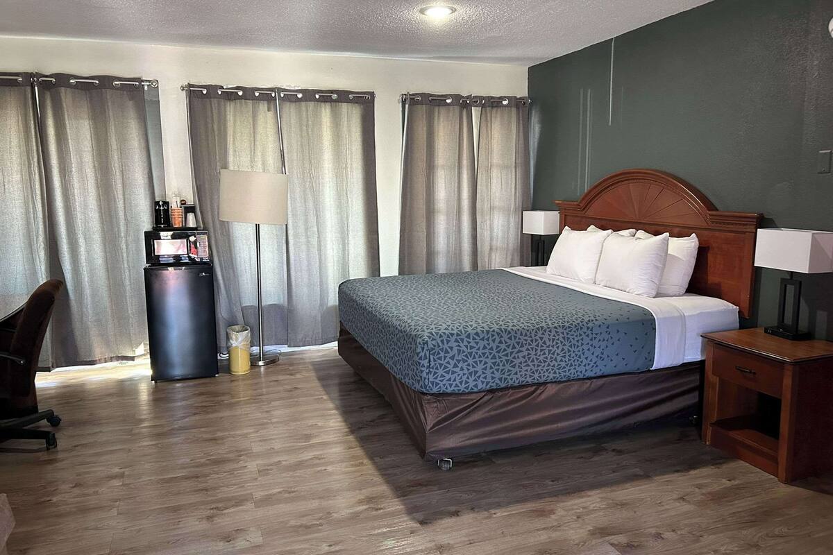 Ein Hotelzimmer mit Bett, Nachttischen, Schreibtisch, Lampe und Vorhängen.