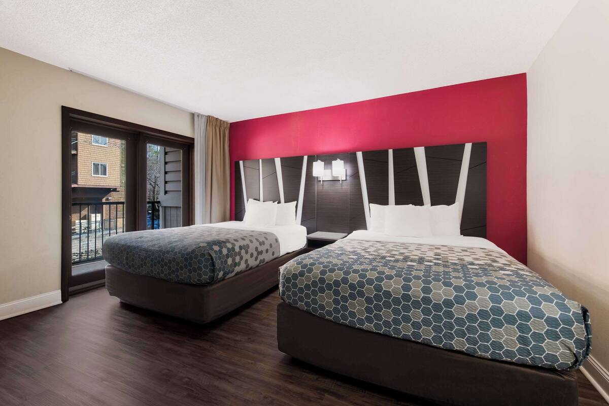 Ein Hotelzimmer mit zwei Betten, einer roten Akzentwand und Blick auf den Balkon.