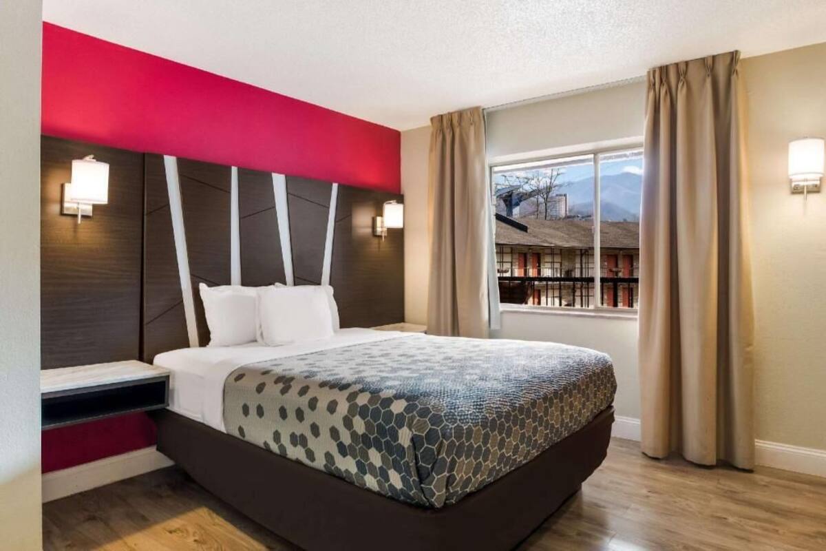 Ein Hotelzimmer mit Bett, Fenster mit Vorhängen und Blick auf ein Gebäude.