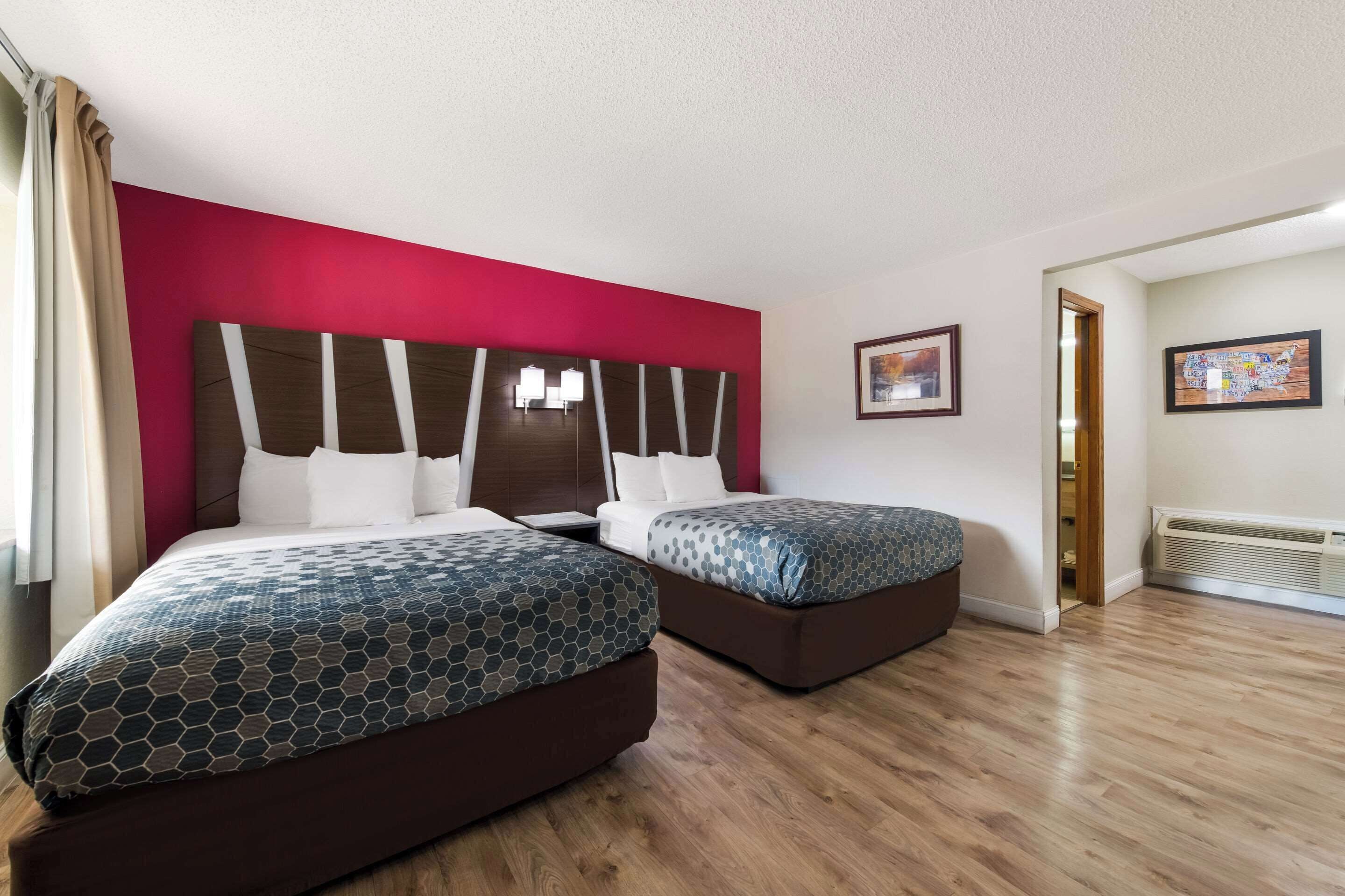 A hotel room with two beds, a red accent wall, and a wooden floor.