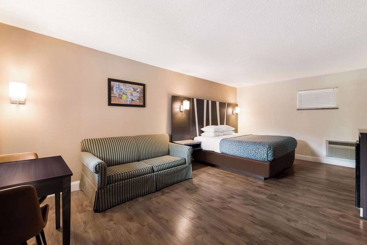 Ein Hotelzimmer mit einem Bett, einer gestreiften Couch, einem kleinen Tisch und einer Wandlampe.