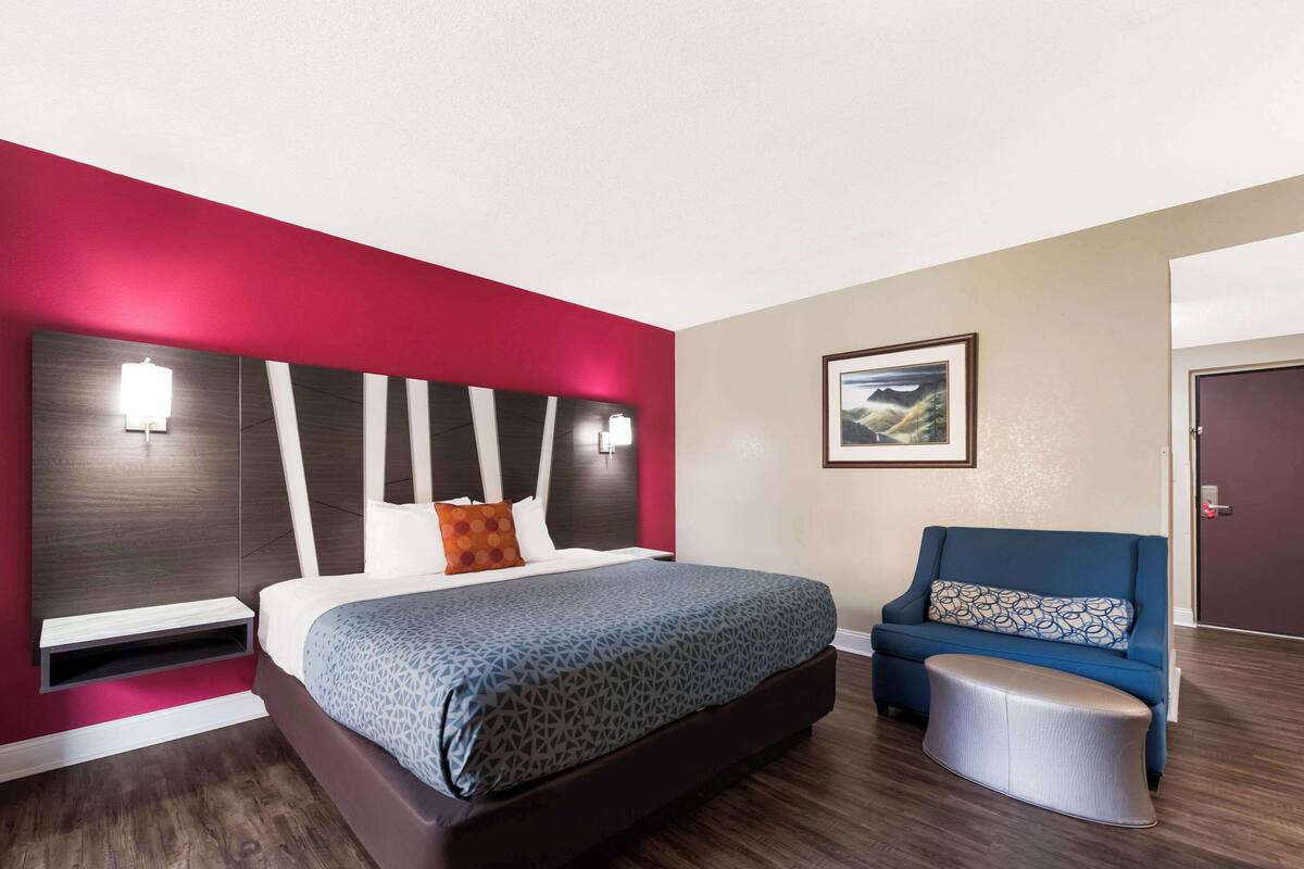 Ein modernes Hotelzimmer mit einem großen Bett, einem blauen Sofa und einem kleinen Hocker.