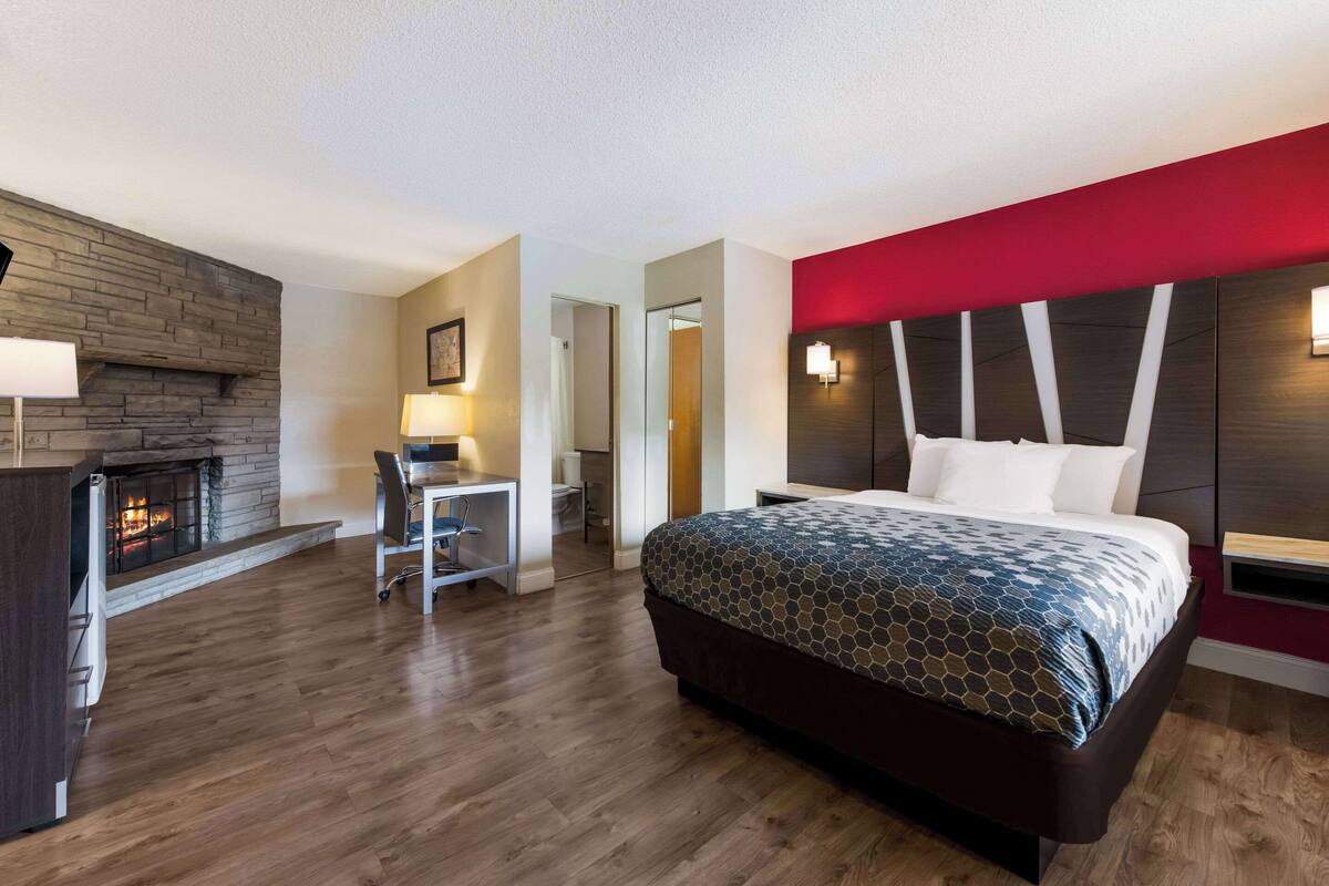 Ein Hotelzimmer mit einem Bett, einem Schreibtisch, einem Sessel, einem Kamin und einer roten Akzentwand.
