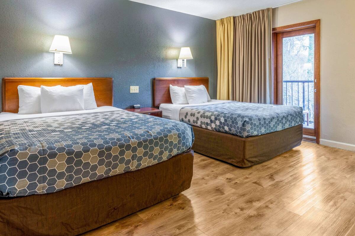 Ein Hotelzimmer mit zwei Betten, Holz-Kopfteilen und einem Balkon mit Vorhängen.