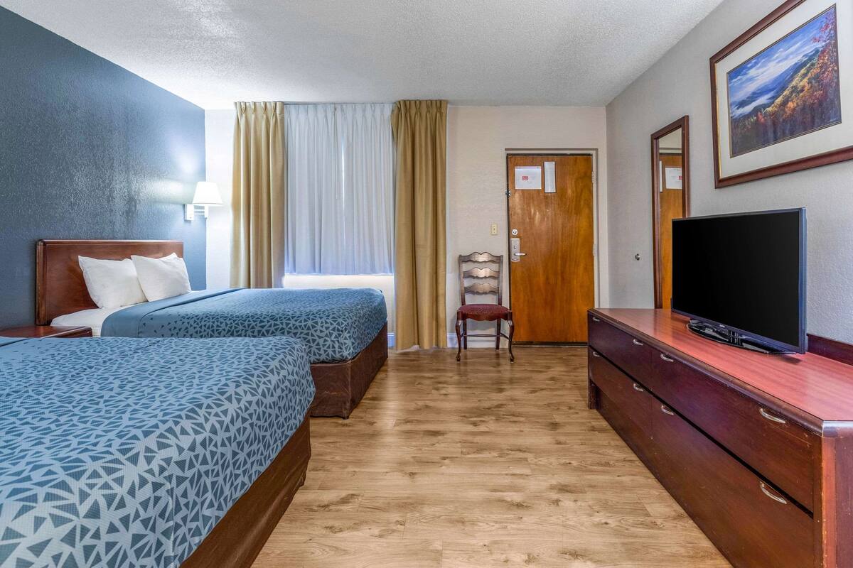 Ein Hotelzimmer mit zwei Betten, einem Fernseher, einem Schminktisch und einem Sessel.