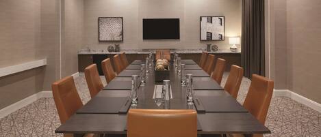 A conference room with a long table, brown leather chairs, a modern chandelier, and framed artwork on the walls.