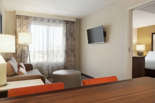 Una habitación de hotel con sofá, reposapiés y una mesa de comedor con sillas.