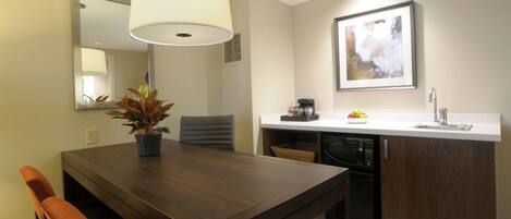 A modern kitchen with a wooden dining table, chairs, a hanging light fixture, a sink, and a microwave.