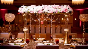 Una mesa de banquete con un centro de flores, candelabros de cristal y un mantel brillante.