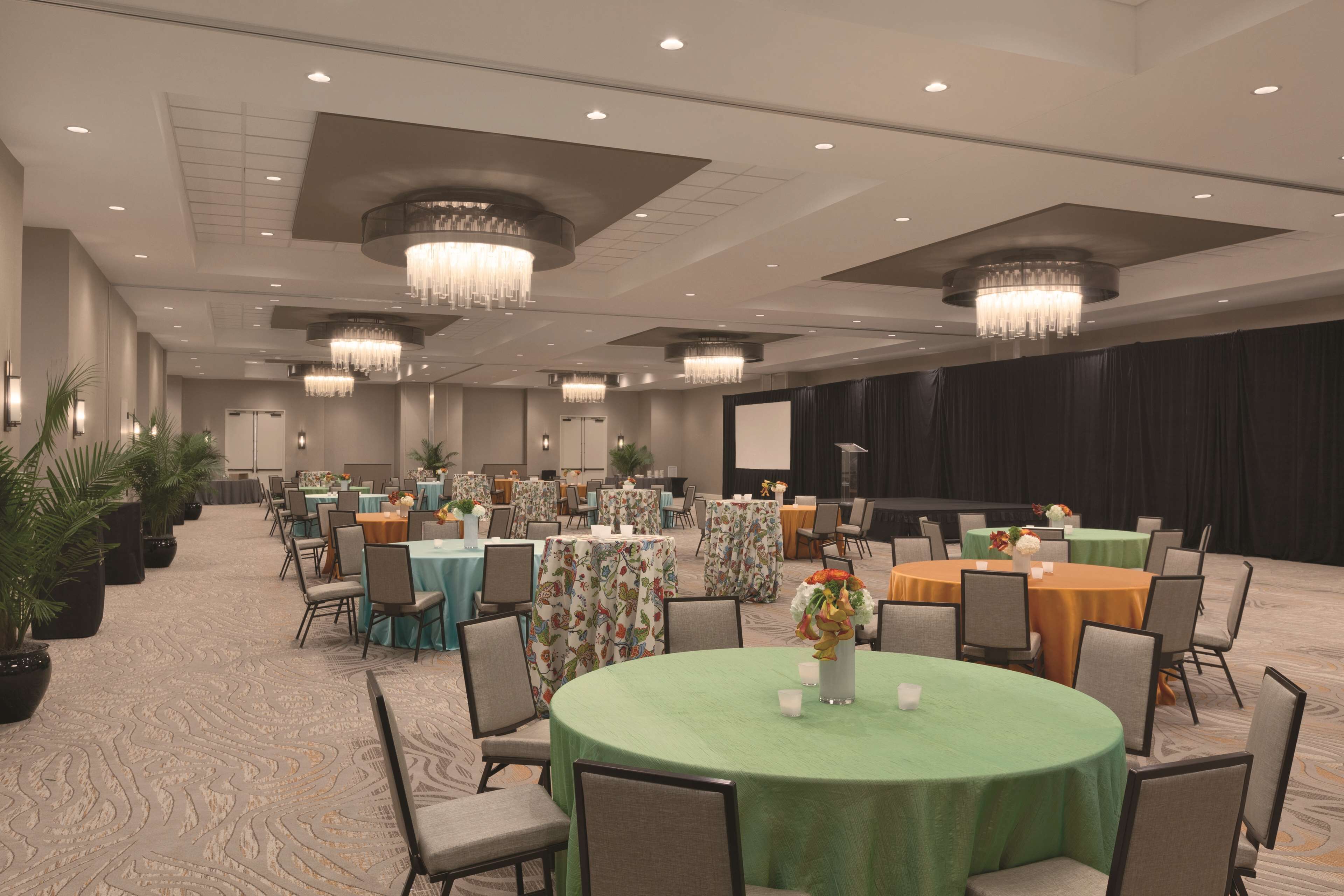A large conference room with round tables, chairs, and chandeliers.
