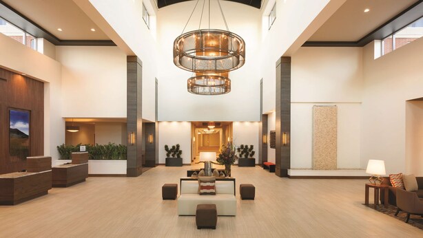 Un hall espacioso con una zona de estar central, un gran candelabro y un mostrador de recepción con plantas.