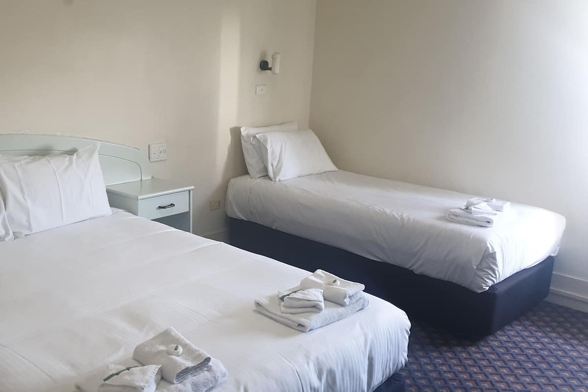 Ein Hotelzimmer mit zwei Betten, jeweils mit weißer Bettwäsche und Kissen, einem kleinen Nachttisch und einer Wandleuchte.