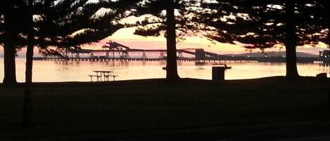 A park with trees, a picnic table, and a bridge in the background.