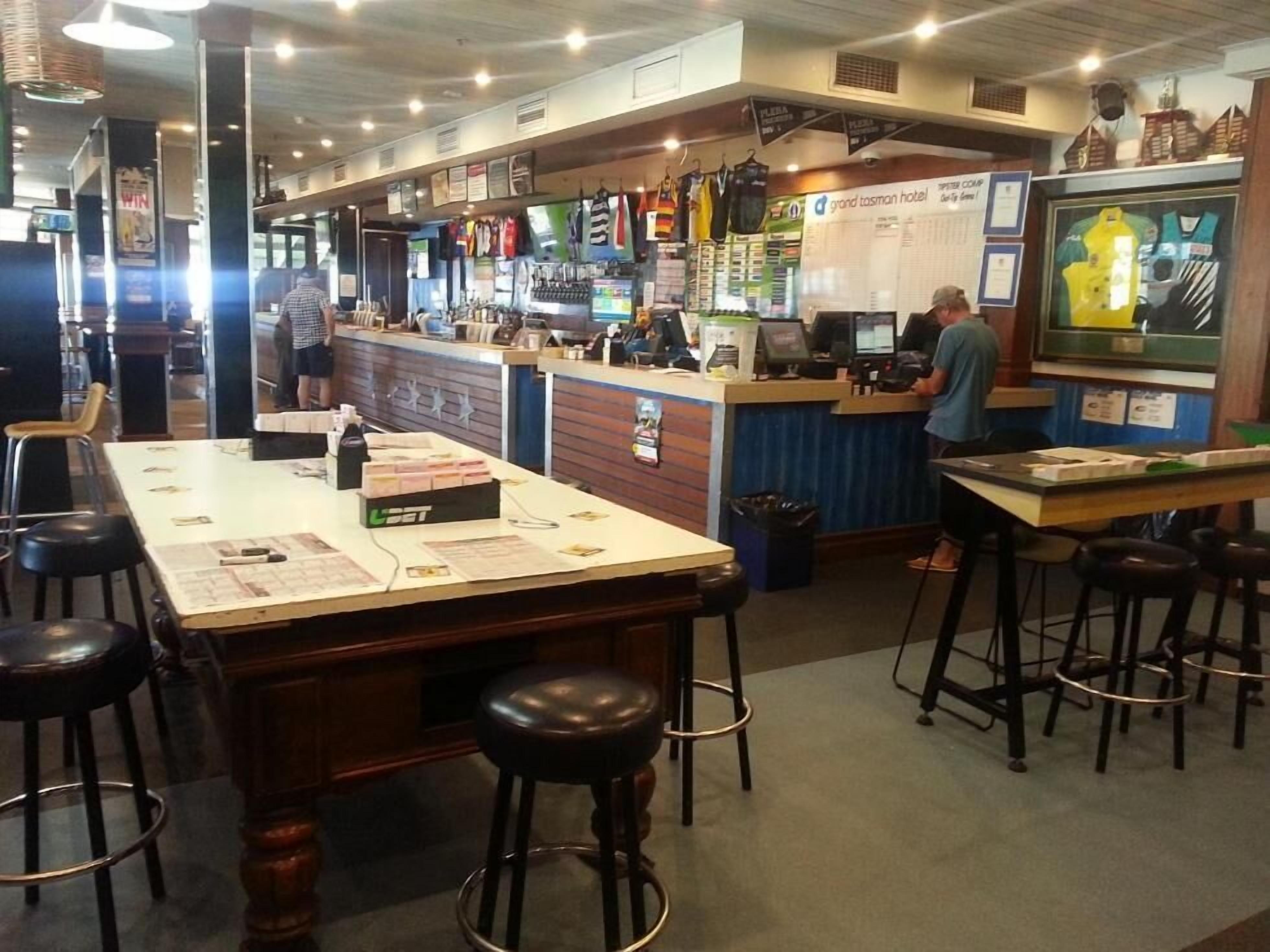 Zona de bar con taburetes, un mostrador con caja registradora y una exhibición de camisetas deportivas.
