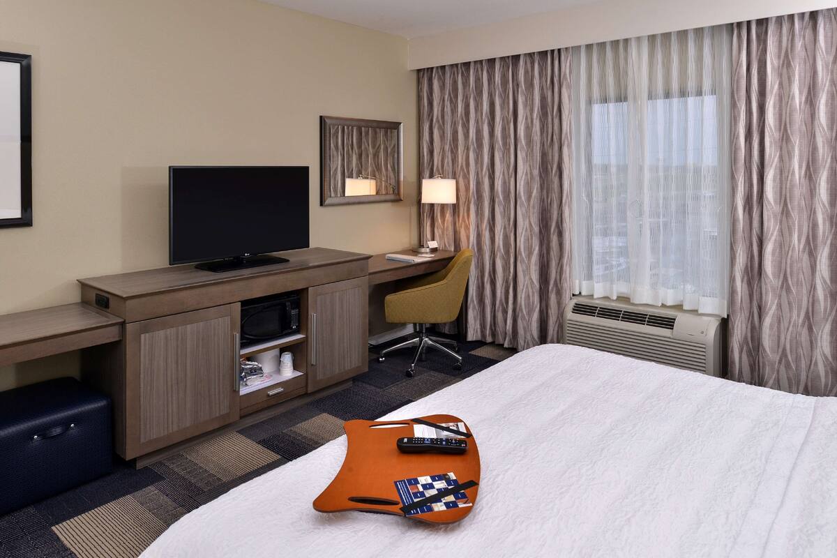 Ein Hotelzimmer mit einem Bett, einem Schreibtisch mit Fernseher, einem Sessel und einem Koffer.