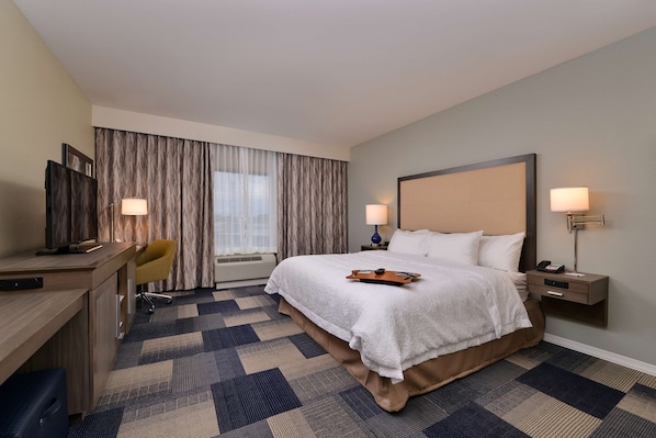 A hotel room with a large bed, a desk with a chair, two bedside lamps, and a window with curtains.