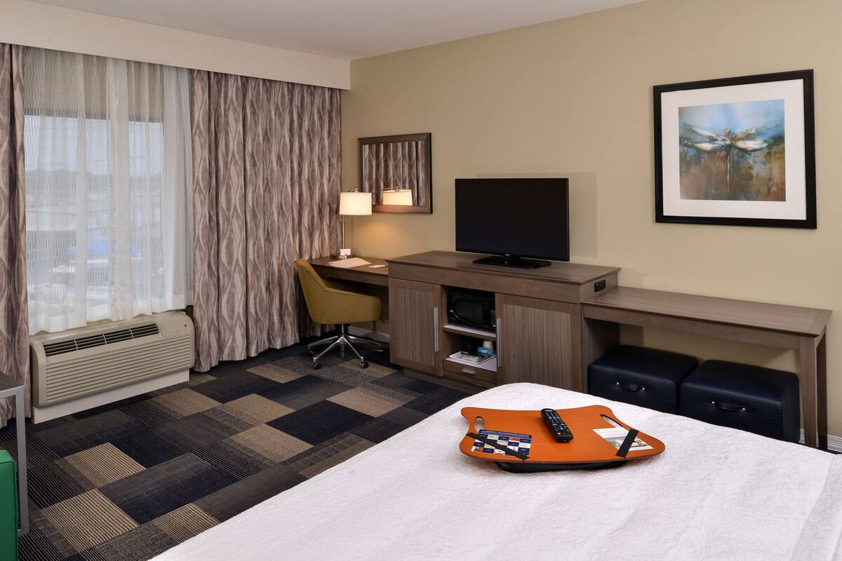 Ein Hotelzimmer mit Bett, Schreibtisch, Stuhl, Fernseher und einem gerahmten Bild an der Wand.