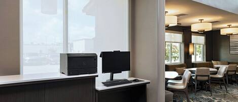 A hotel room with a desk, printer, computer, and seating area with tables and chairs.