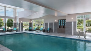 Une piscine intérieure à l’eau d’un bleu cristallin, entourée de chaises longues et d’un mur en pierre.