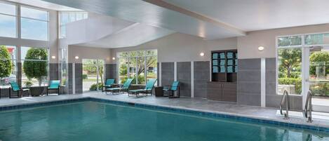 An indoor swimming pool with clear blue water, surrounded by lounge chairs and a stone wall.
