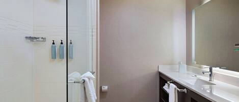 A modern bathroom with a glass shower enclosure, a large mirror, and a vanity with a sink and towel rack.