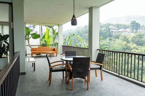 A balcony with a table and chairs, a sofa, and a hanging light fixture. - Green Forest Plantation View 6BR with Infinity Pool (Cimenyan)