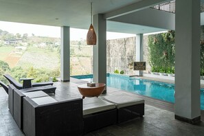 A poolside area with a view of the landscape, a hanging light fixture, and a sign. - Green Forest Plantation View 6BR with Infinity Pool (Cimenyan)