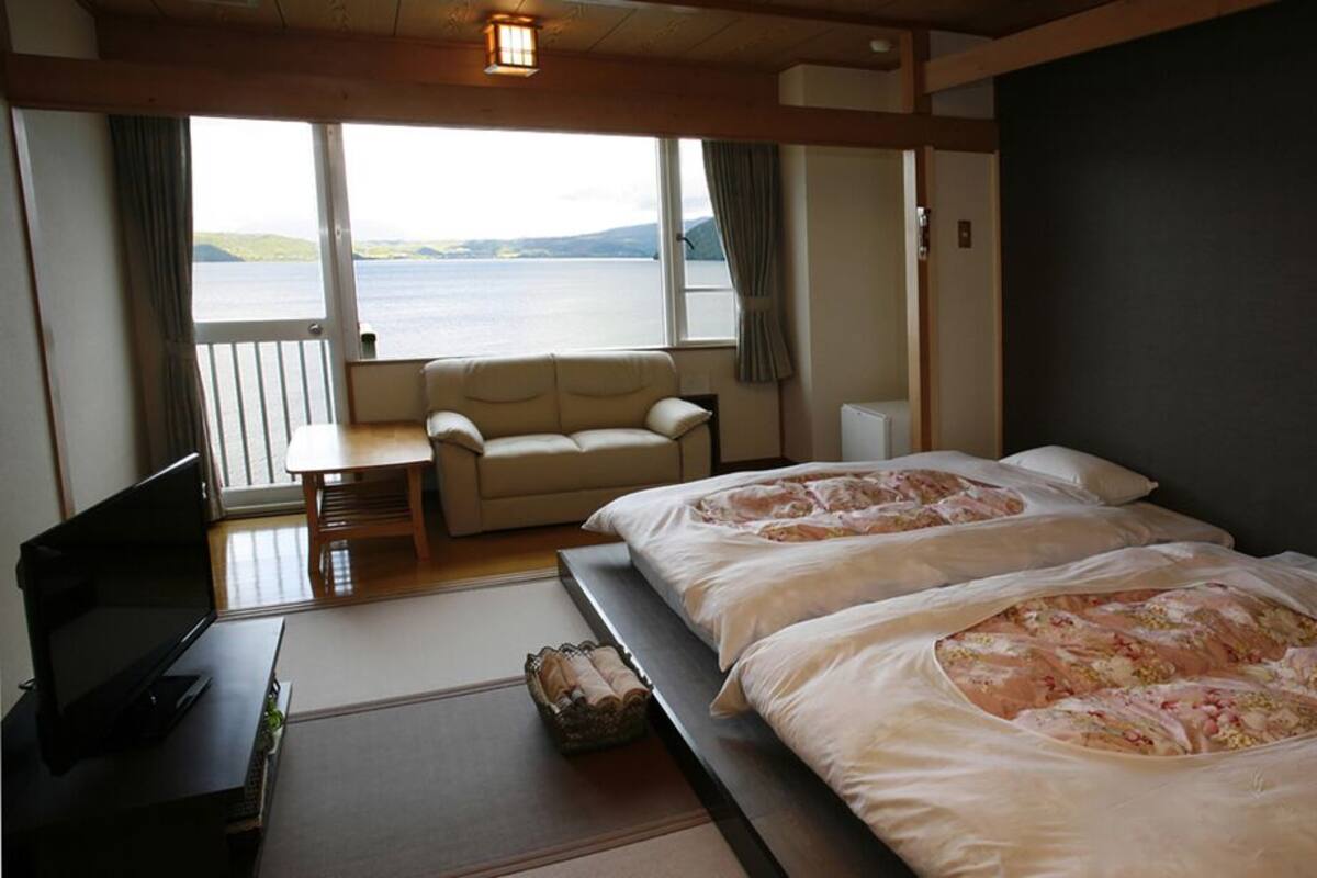 Une chambre d’hôtel avec deux lits, un canapé, une télévision et une vue sur la mer.
