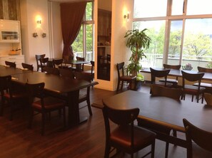 A dining area with multiple tables and chairs, large windows with curtains, and a potted plant. - Granvillage Toya Daiwa Ryokan Annex (Toyako)