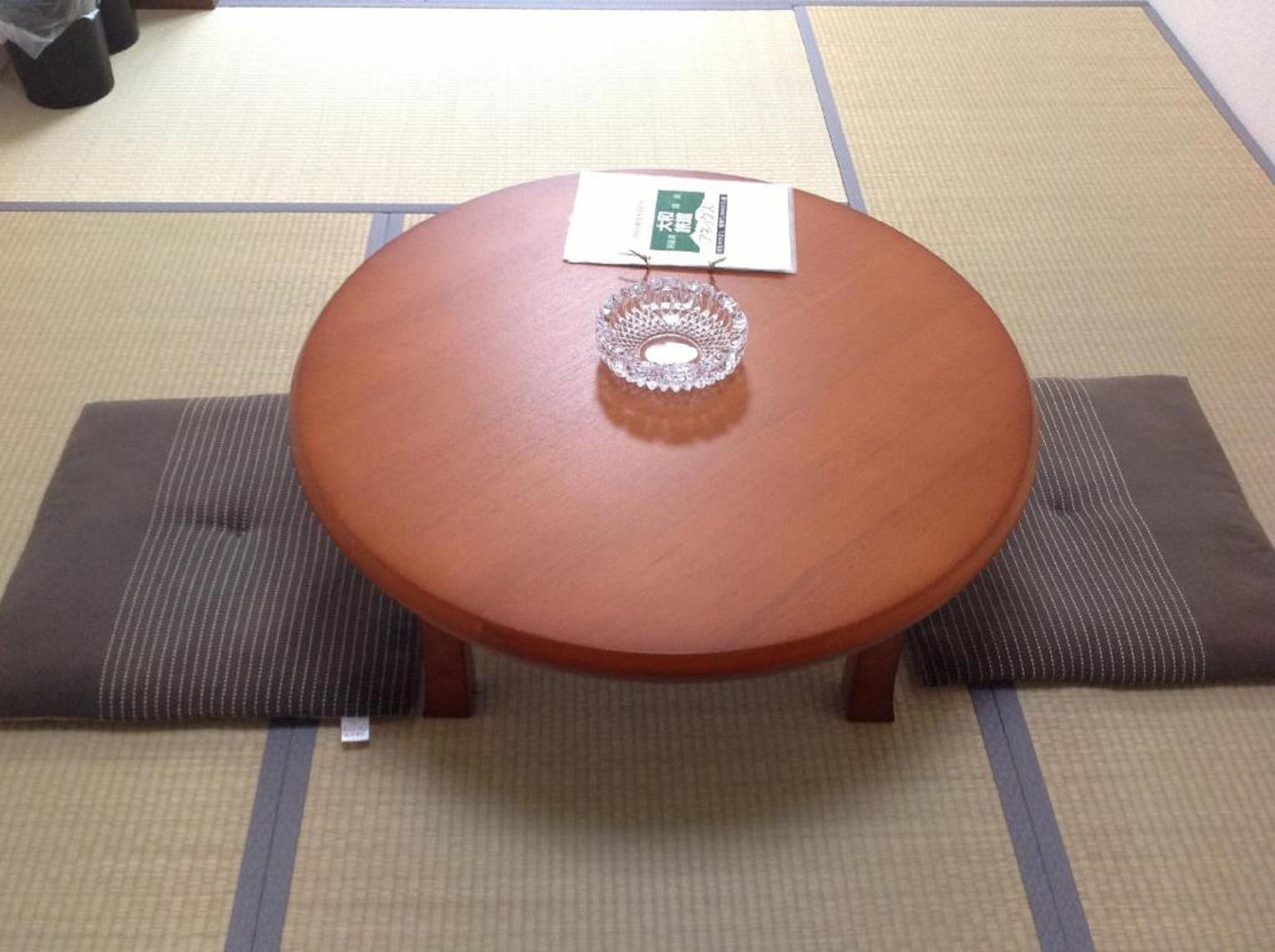 Una mesa redonda de madera con un centro decorativo de metal, colocada sobre esteras de tatami.