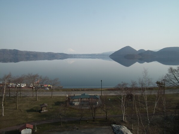 Un lago tranquilo con montañas al fondo, un pabellón y un pequeño edificio cerca de la orilla.