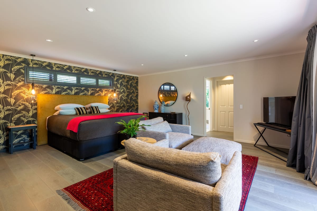Ein modernes Schlafzimmer mit einem Bett, einem grauen Sofa, einem roten Teppich und einem Fernseher in der Ecke.