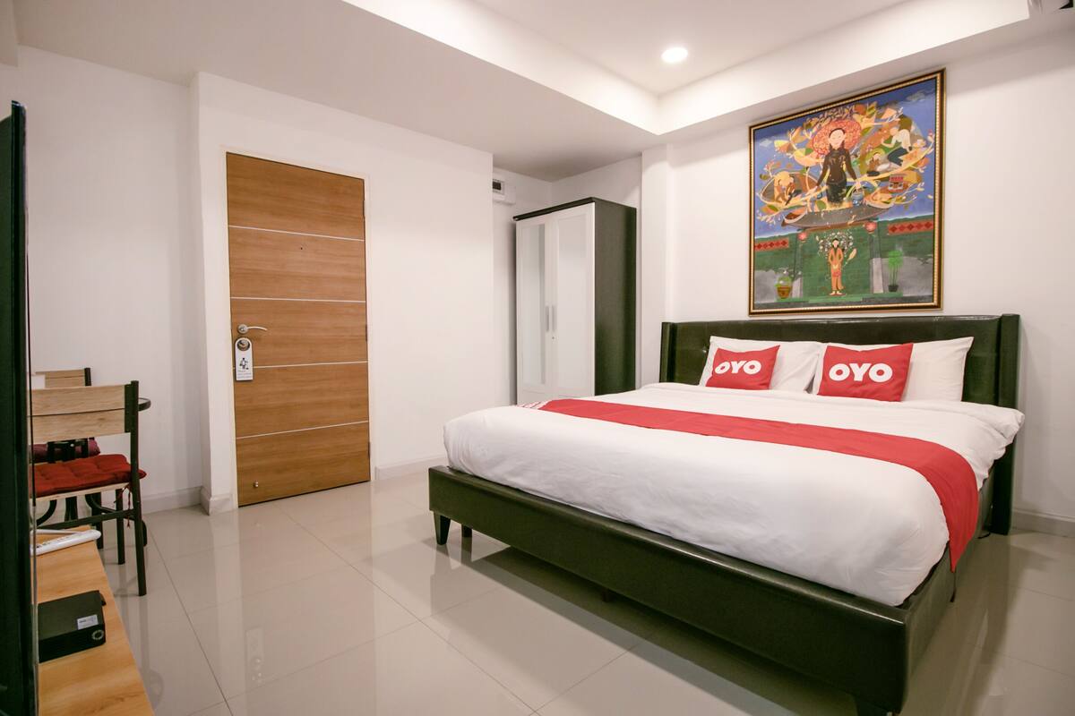 A bedroom with a bed, a wooden chair, a desk, and a wardrobe.