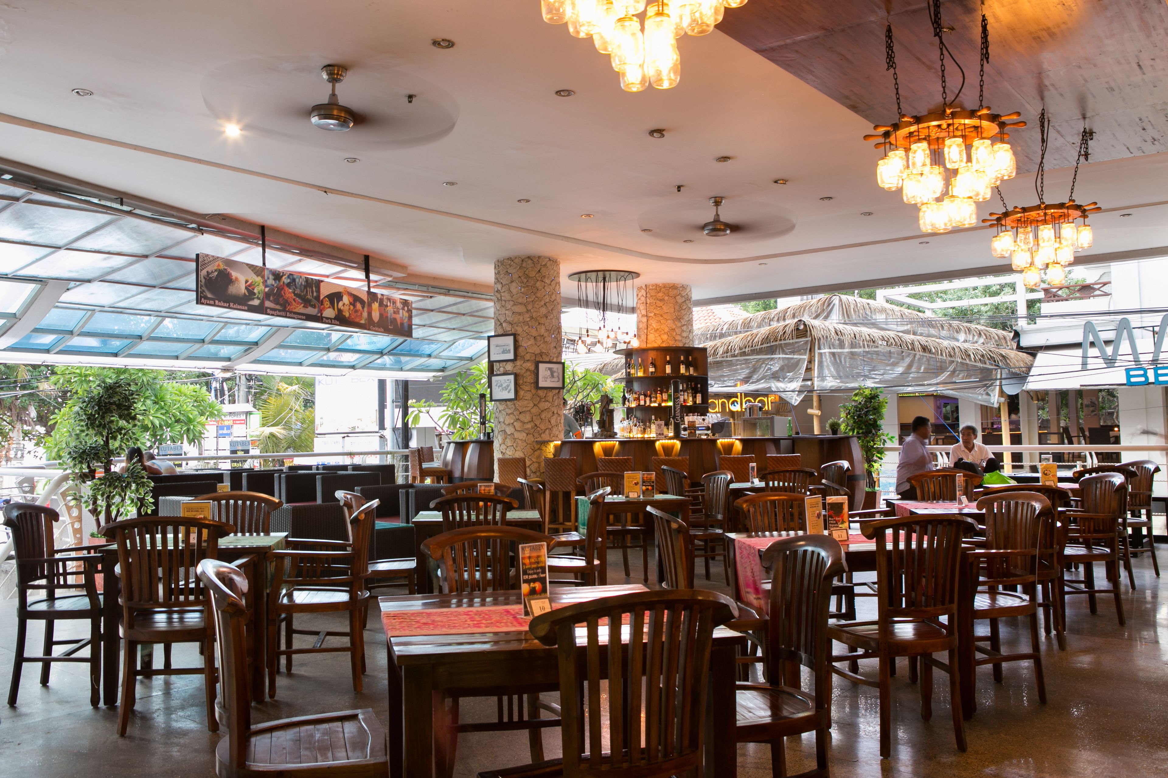 A spacious restaurant with wooden furniture, a bar area, and a view of the outdoors through large windows.