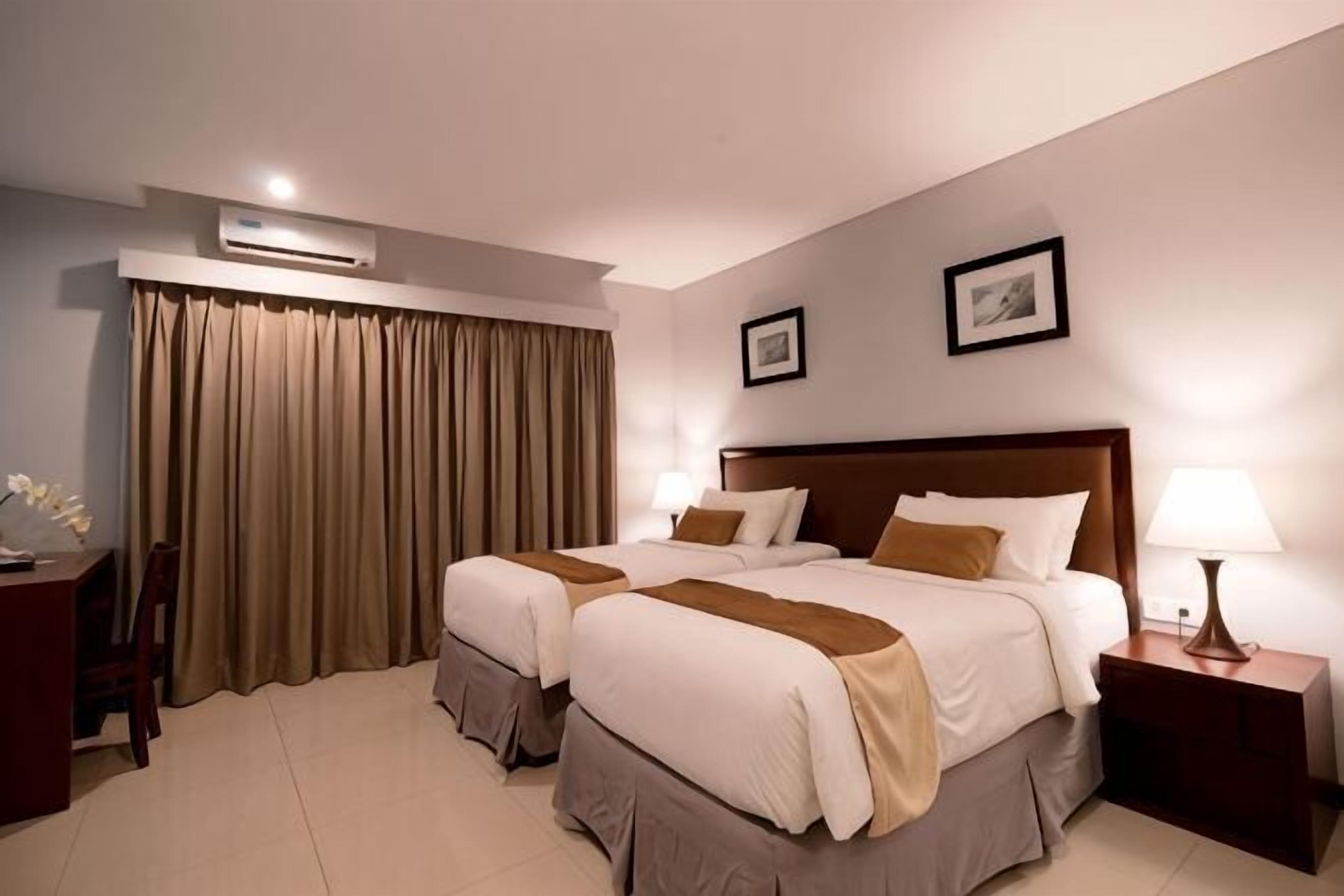 A hotel room with two beds, a desk, a chair, a lamp, and a picture on the wall.