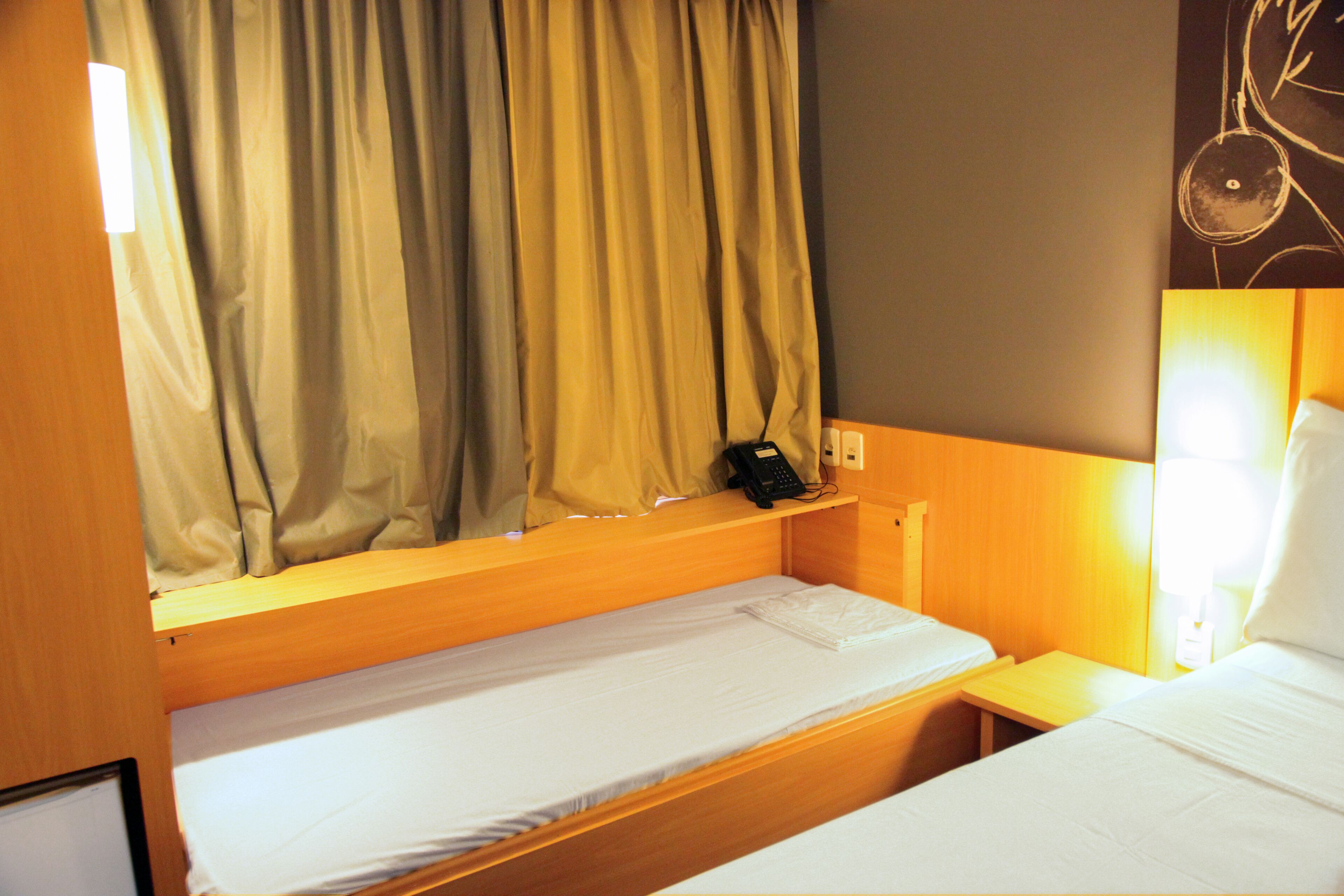 A hotel room with two single beds, a bedside table with a phone, and a curtain covering the window.