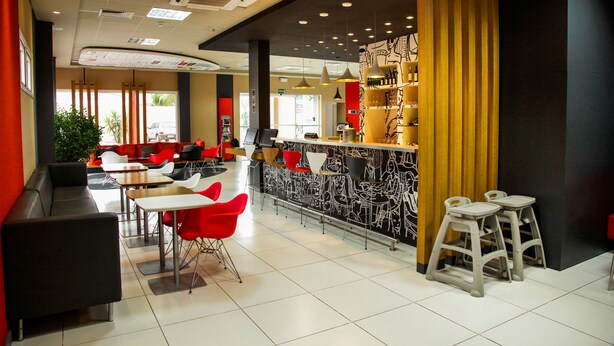 A modern cafe with a bar area, seating arrangements, and a decorative wall. - ibis Bacabal (Bacabal)