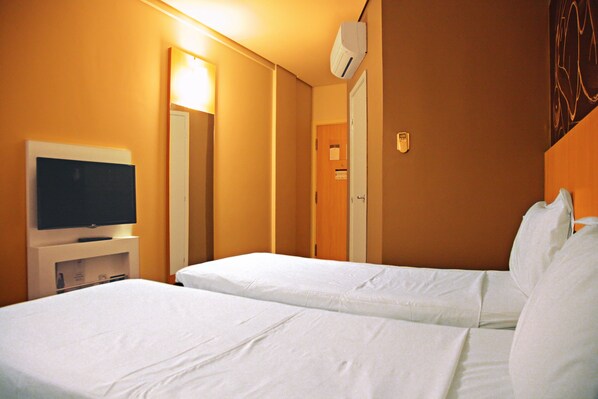 A hotel room with two single beds, a television on a stand, and an air conditioning unit on the wall.
