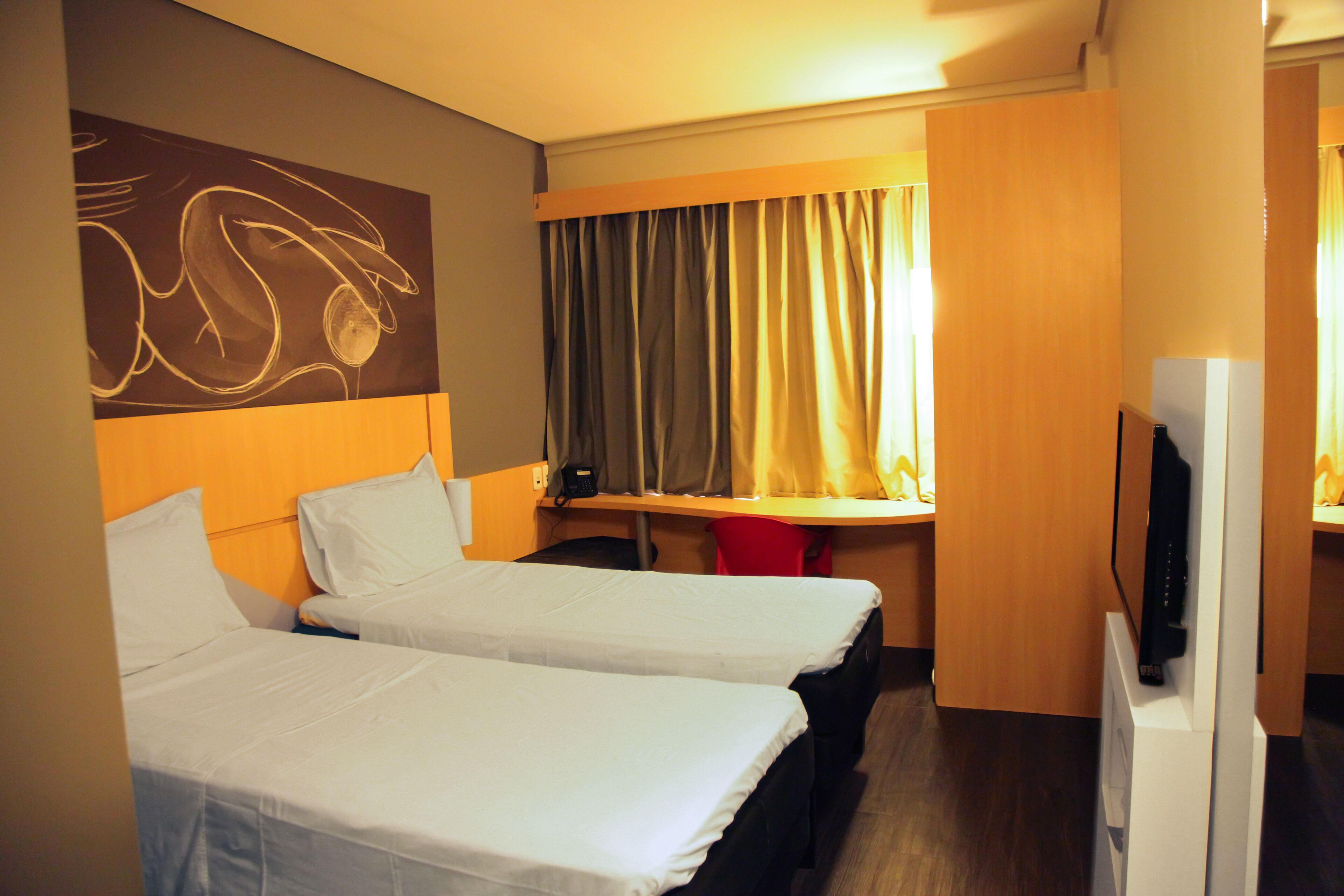 A hotel room with two beds, a desk, a television, and a curtain.