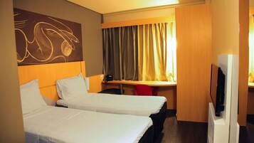 Quarto de hotel com duas camas, uma escrivaninha, uma televisão e uma cortina.