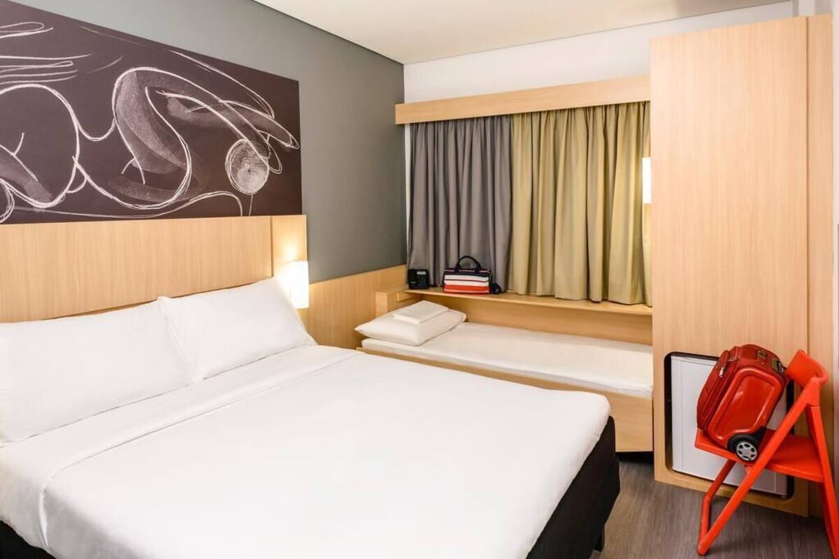 A hotel room with a large bed, a small sofa, a desk with a chair, and a window with curtains.