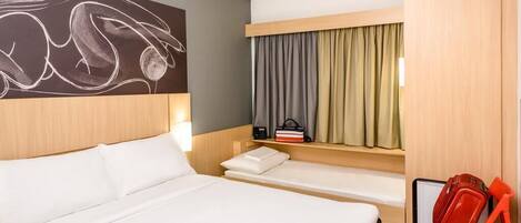 Een hotelkamer met een groot bed, een kleine zithoek, een bureau met stoel en een raam met gordijnen.