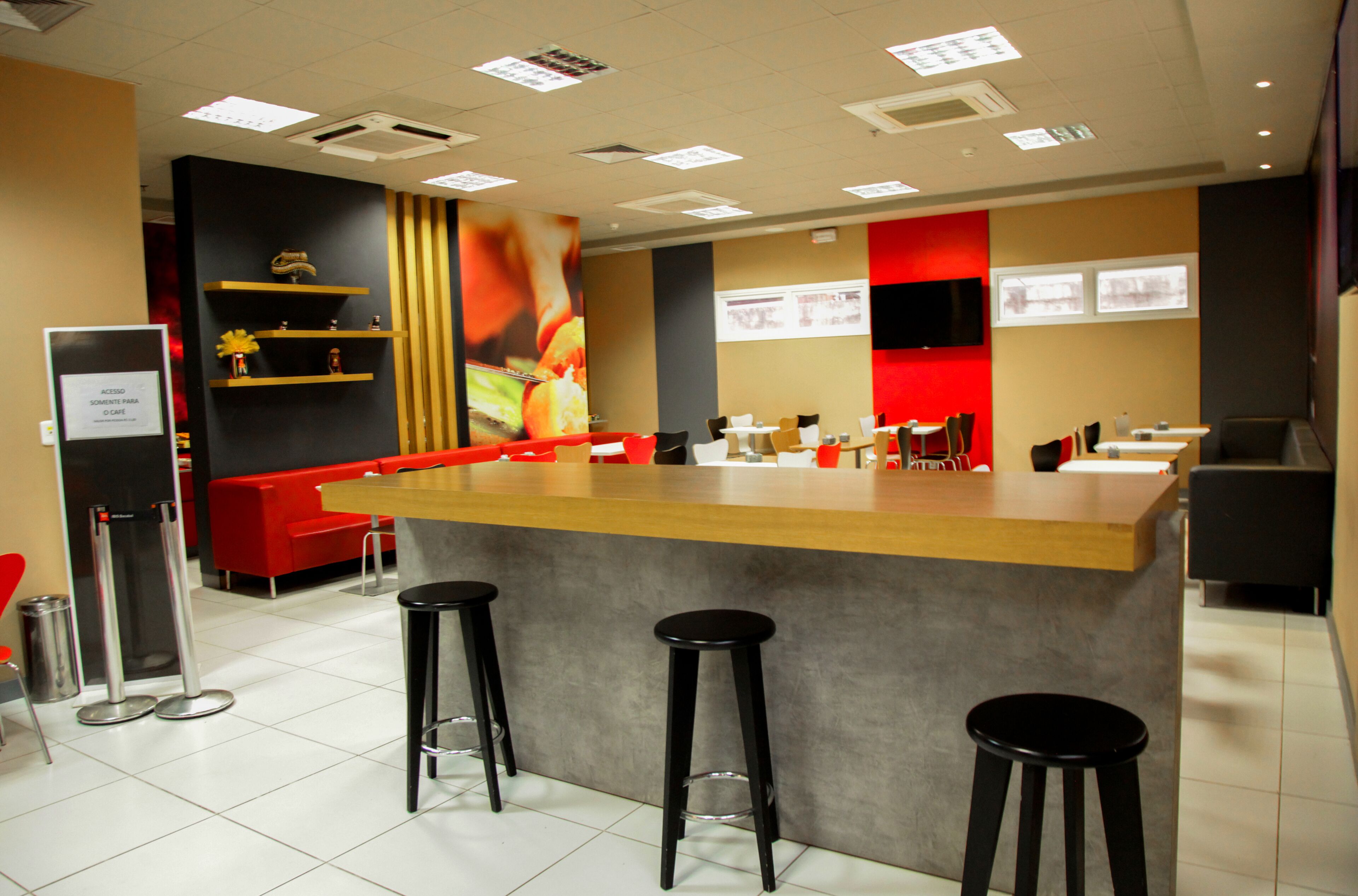 A modern restaurant interior with a central bar, red seating, and a tiled floor.